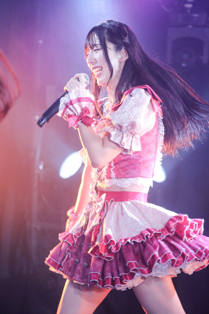 embellir(あんべりー)の水野ひなたちゃんをライブ中に撮影した写真。
目を細めながらとても優しくほほえんでいる。ライブの熱気からか、頬には汗がにじんでおり、照明を受けてキラキラ輝いている。
2025年11月22日 Zirco Tokyo SYNC FESTAにて撮影。