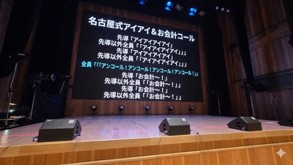 ステージの写真を背景にテキストが埋め込まれている。 名古屋式アイアイ＆お会計コール 先導「アイアイアイアイ」 先導以外全員「「「アイアイアイアイ」」」 先導「アイアイアイアイ」 先導以外全員「「「アイアイアイアイ」」」 全員「「「「アンコール！アンコール！アンコール！アンコール！」」」」 先導「お会計～！」 先導以外全員「「「お会計～！」」」 先導「お会計～！」 先導以外全員「「「お会計～！」」」