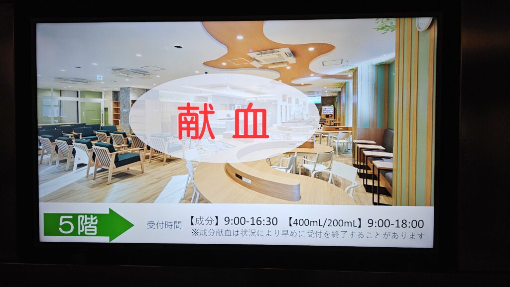 献血と大きく書かれ、開設時間等の情報が表示されているデジタルサイネージ。