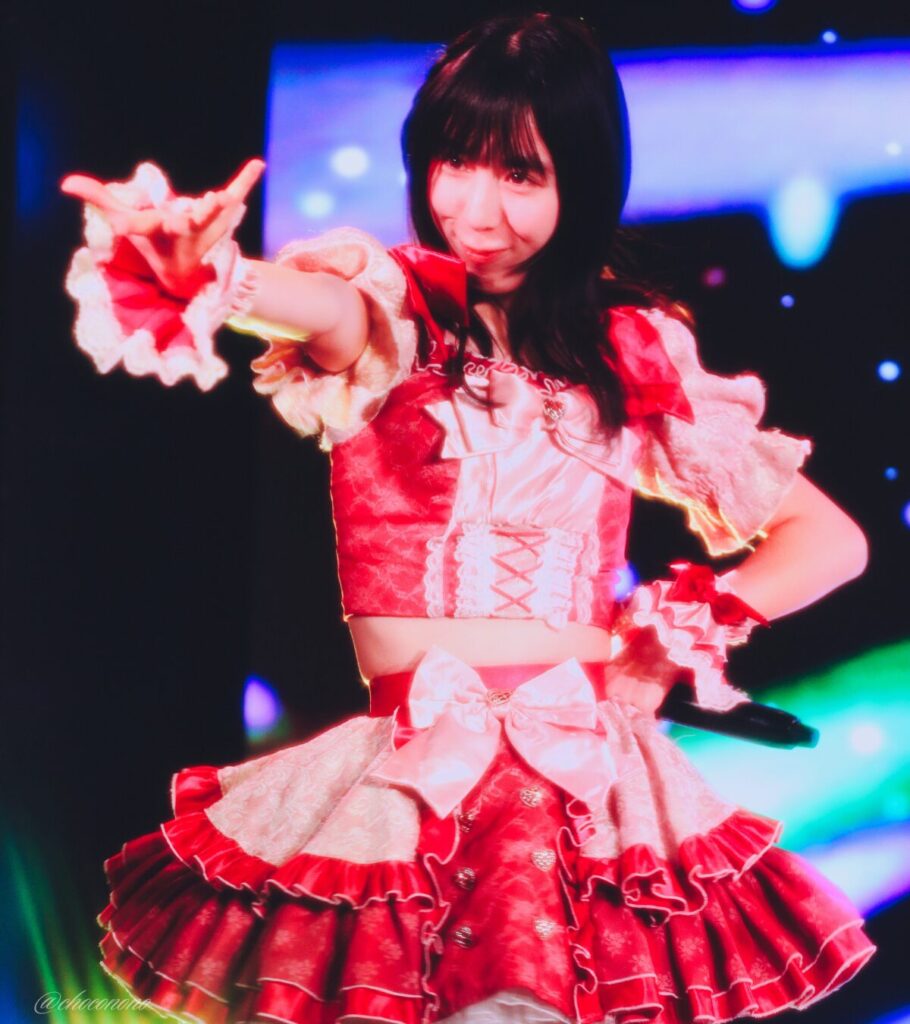 embellir(あんべりー)の水野ひなた(みずのひなた)ちゃんを最前列0番の位置からライブ中に撮影した写真。 ひなたちゃんはストレートヘアーをベースに一束髪を編んでいる。 しっちゃかめっちゃかパラダイスの「みんなといればなんとかなるさ」の歌詞に合わせて手を差しのべるジェスチャーをしている。 2026年3月15日中野坂上S.U.B Tokyo　妃Fesにて撮影。