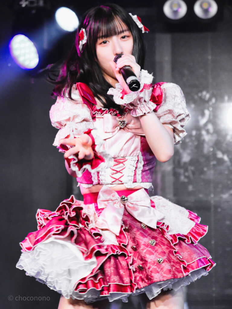 embellir(あんべりー)の水野ひなた(みずのひなた)ちゃんを最前列下手1番の位置からライブ中に撮影した写真。 毛先を巻いて赤いリボンで飾り付けている。 ダンスしながらこちらに手を差しのべてくれている。 2026年3月10日GOTANDA G4　無銭ぷろじぇくと!!にて撮影