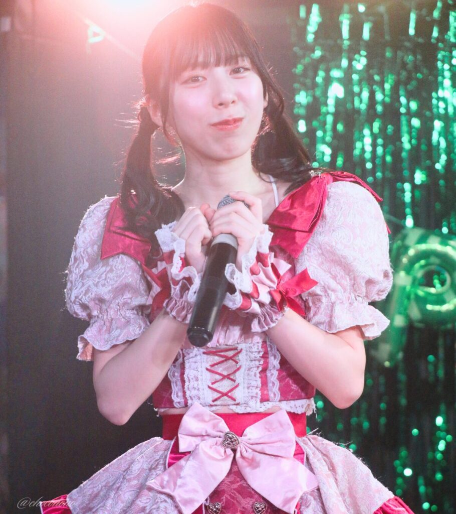 embellir(あんべりー)の水野ひなた(みずのひなた)ちゃんを最前列0番の位置からライブ中に撮影した写真。 ひなたちゃんはこの日の主役の七瀬ましろちゃんをリスペクトして先端をやや巻いたツインテールをしている。 MC中、にこにこした表情でこちらを見つめてくれている。 2026年3月22日　神田CLUB F♯　七瀬ましろ生誕祭2026 ～ねぇねぇ教えて！ましろ、今日も可愛い？～にて撮影。