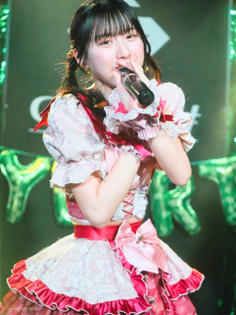 embellir(あんべりー)の水野ひなた(みずのひなた)ちゃんを最前列0番の位置からライブ中に撮影した写真。 ひなたちゃんはこの日の主役の七瀬ましろちゃんをリスペクトして先端をやや巻いたツインテールをしている。 フツーに奇跡!!の「ずっと　ずっとずっと」の歌詞に合わせて自分の肩を抱いて前後するダンス中。 2026年3月22日　神田CLUB F♯　七瀬ましろ生誕祭2026 ～ねぇねぇ教えて！ましろ、今日も可愛い？～にて撮影。