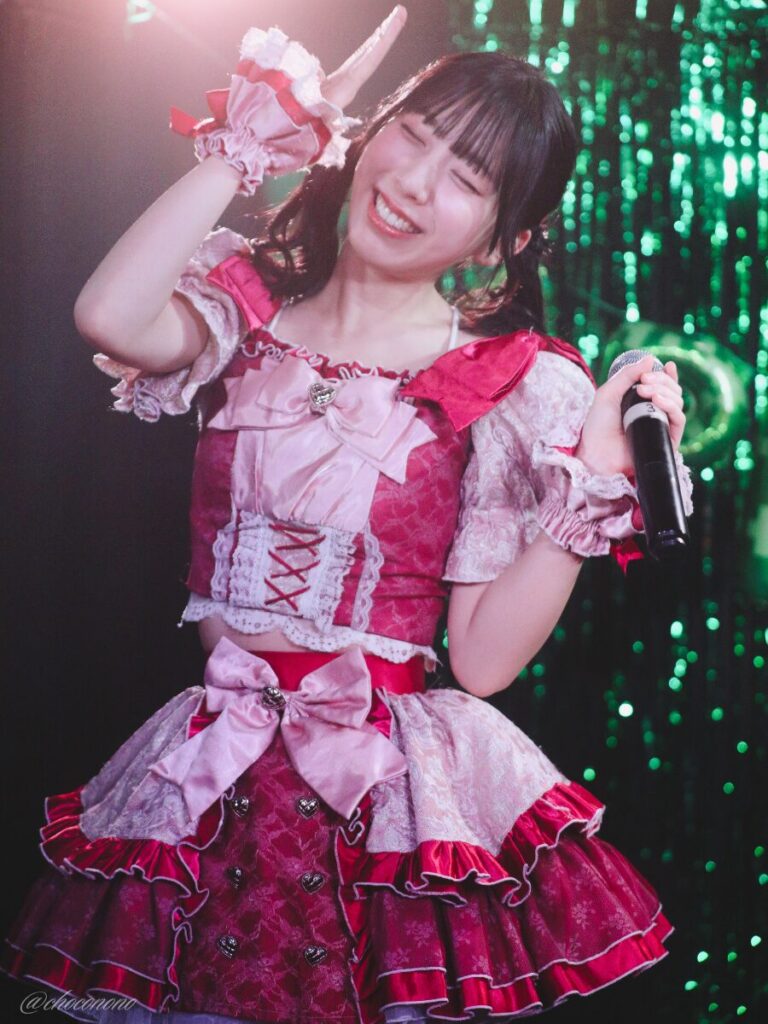 embellir(あんべりー)の水野ひなた(みずのひなた)ちゃんを最前列0番の位置からライブ中に撮影した写真。 ひなたちゃんはこの日の主役の七瀬ましろちゃんをリスペクトして先端をやや巻いたツインテールをしている。 MC中、自分の頭の上あたりに手を置いてにこにこ笑っている。なでなでポーズだろうか。 2026年3月22日　神田CLUB F♯　七瀬ましろ生誕祭2026 ～ねぇねぇ教えて！ましろ、今日も可愛い？～にて撮影。