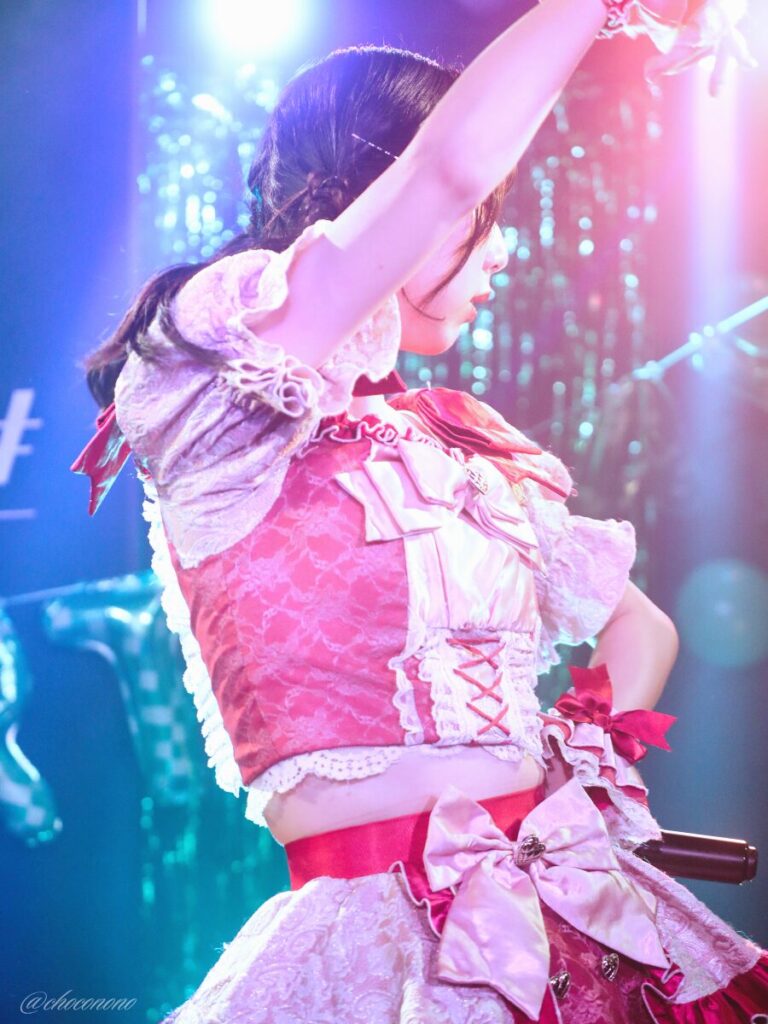 embellir(あんべりー)の水野ひなた(みずのひなた)ちゃんを最前列0番の位置からライブ中に撮影した写真。 ひなたちゃんはこの日の主役の七瀬ましろちゃんをリスペクトして先端をやや巻いたツインテールをしている。 ダンスの途中振り上げた腕で顔は半分隠れているが、その横顔がとても美しい。照明もあいまって、光の中で舞う女神のようだ。 2026年3月22日　神田CLUB F♯　七瀬ましろ生誕祭2026 ～ねぇねぇ教えて！ましろ、今日も可愛い？～にて撮影。