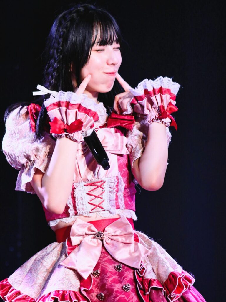 embellir(あんべりー)の水野ひなた(みずのひなた)ちゃんを最前列0番の位置からライブ中に撮影した写真。 ひなたちゃんはストレートヘアーに編み込みをしている。 両手の人差し指をほっぺたにくっつけて目を細めてにこにこしている。 2026年3月28日中野坂上S.U.B Tokyo Tune JACKにて撮影。