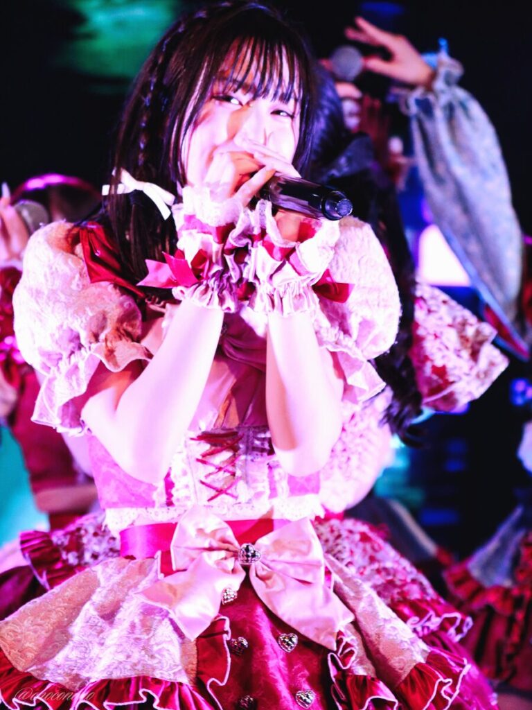 embellir(あんべりー)の水野ひなた(みずのひなた)ちゃんを最前列0番の位置からライブ中に撮影した写真。 ひなたちゃんはストレートヘアーに編み込みをしている。 マイクを大事そうに構えて歌唱しながらこちらに微笑みかけてくれている。 2026年3月28日中野坂上S.U.B Tokyo Tune JACKにて撮影。