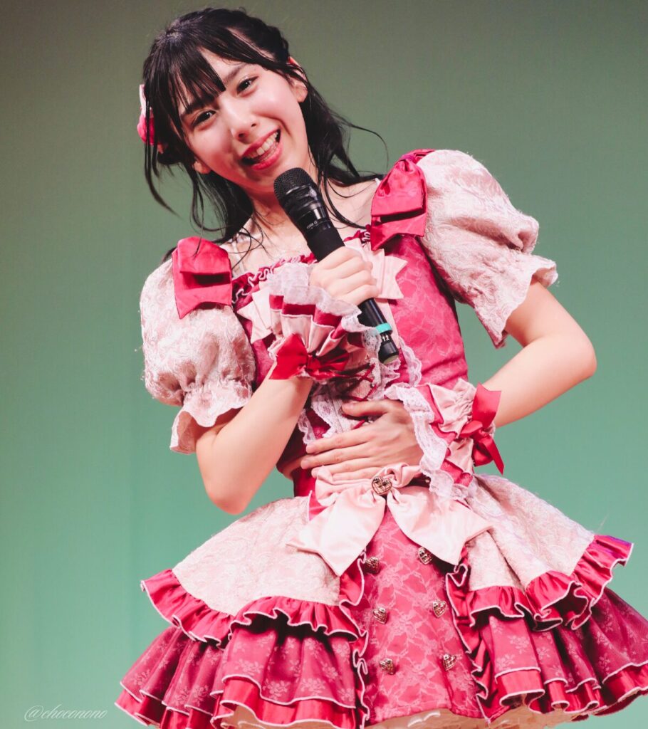 embellir(あんべりー)の水野ひなた(みずのひなた)ちゃんを最前列0番の位置からライブ中に撮影した写真。 ひなたちゃんは編み込みにくるみちゃんヘアー。衣装のイメージにぴったりなベリーカラーのリボンをしている。 MC中、こちらをのぞき込むようにしながらにこにこと見つめてくれている。 2026年4月4日なかのZERO小ホール IDOL SODA Stream!!にて撮影。