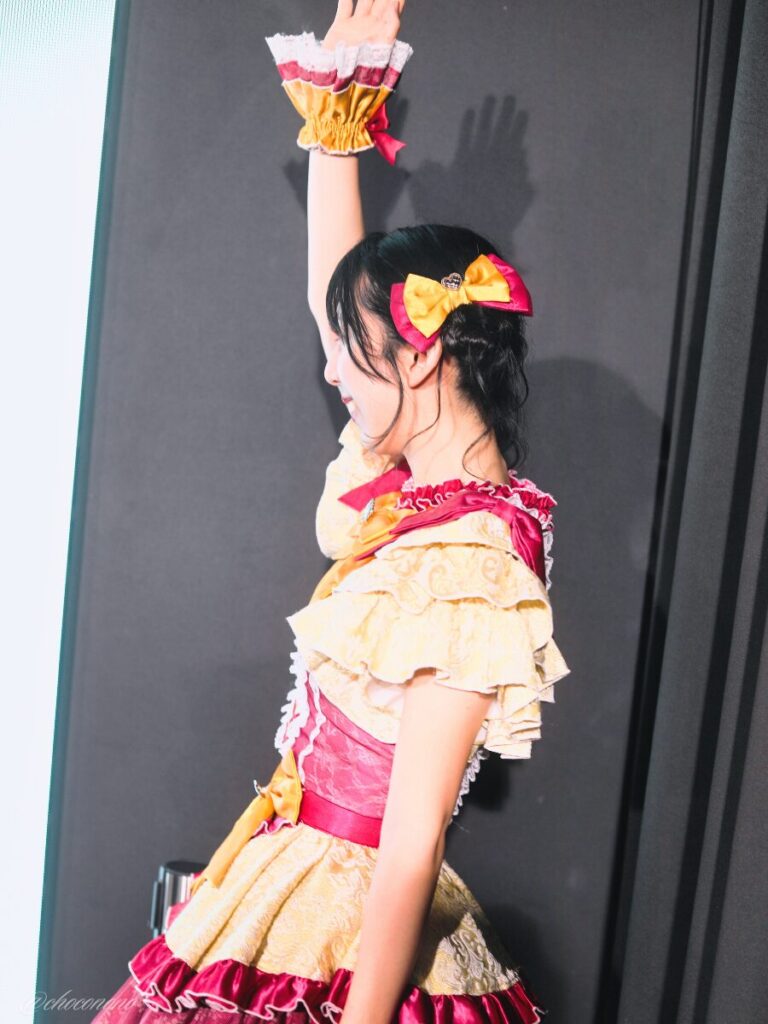 embellir(あんべりー)の水野ひなた(みずのひなた)ちゃんを特典会で撮らせてもらったソロショット写真。 ひなたちゃんは普段と衣装を交換してきいろ色の衣装。お団子からちょろちょろとしっぽが出ているような髪型。 未熟なプリンセスの冒頭の片手を挙げて「始めます」のポーズ。 2026年4月9日SHIBUYA ONE5 embellir主催ライブにて撮影。