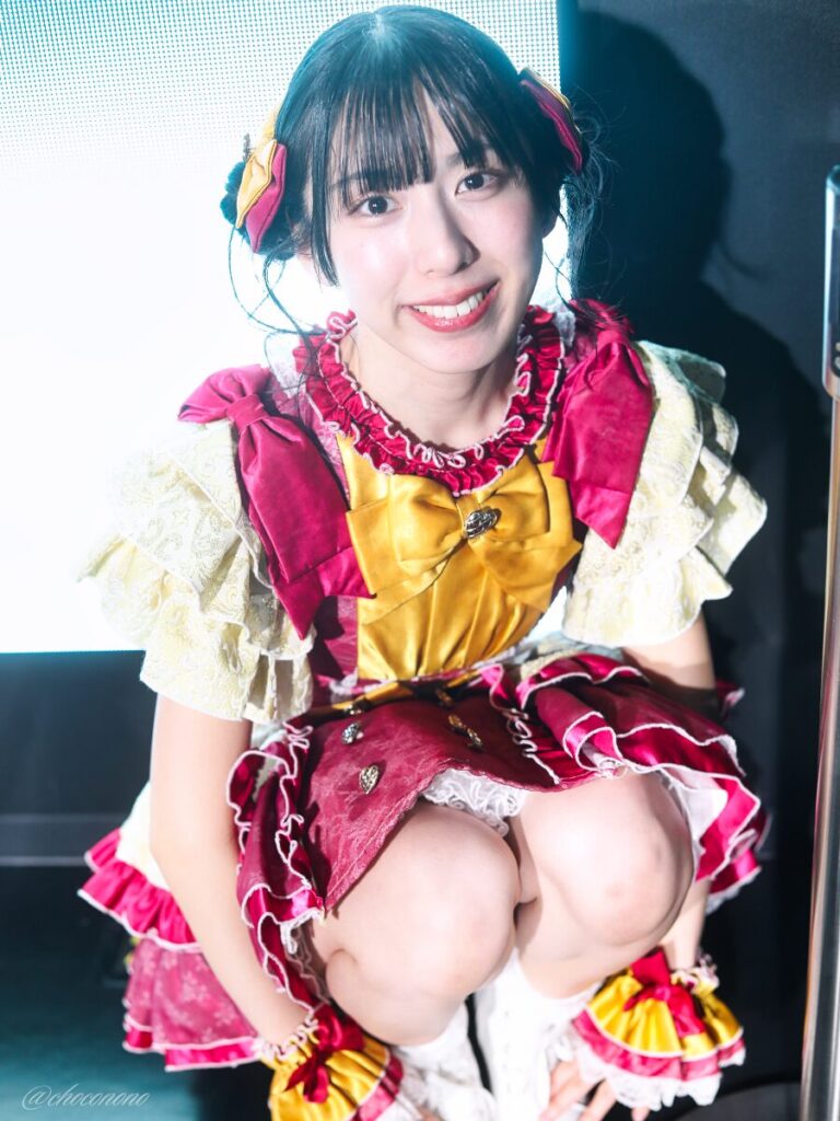 embellir(あんべりー)の水野ひなた(みずのひなた)ちゃんを特典会で撮らせてもらったソロショット写真。 ひなたちゃんは普段と衣装を交換してきいろ色の衣装。お団子からちょろちょろとしっぽが出ているような髪型。 しゃがんでこちらをにこにこ見つめてくれている。 2026年4月9日SHIBUYA ONE5 embellir主催ライブにて撮影。