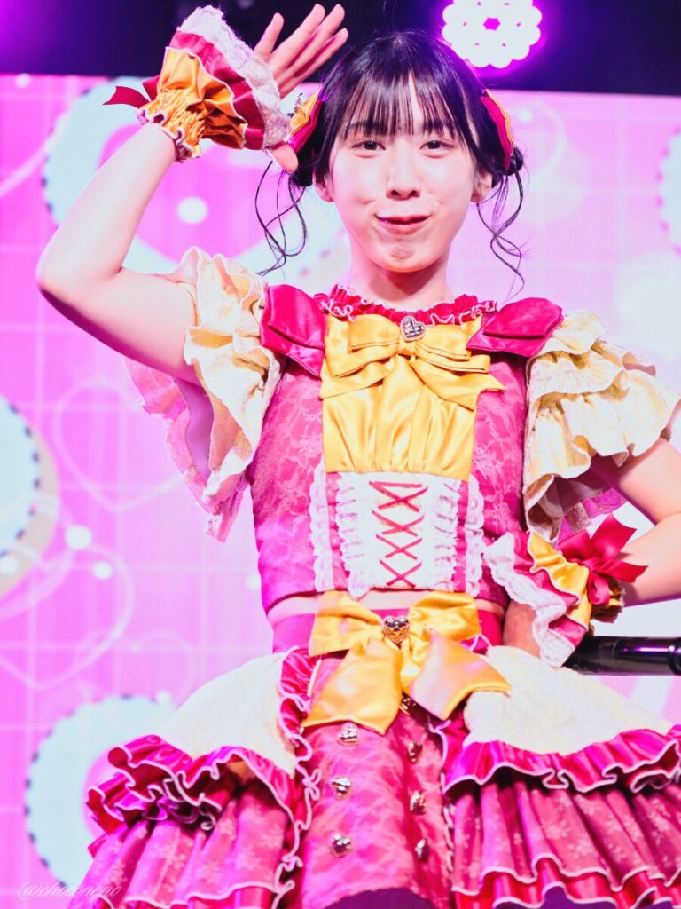 embellir(あんべりー)の水野ひなた(みずのひなた)ちゃんを最前列下手2番あたりからライブ中に撮影した写真 ひなたちゃんは普段と衣装を交換してきいろ色の衣装。お団子からちょろちょろとしっぽが出ているような髪型。 敬礼のようなポーズをしてにこにことこちらを見つめてくれている。 2026年4月9日SHIBUYA ONE5 embellir主催ライブにて撮影。