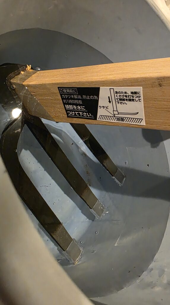 備中鍬の説明書き、「がたつき防止のため使用前に頭部を約1時間程度水に浸けてください」と書いてある。