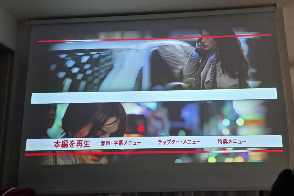 プロジェクターを使ってスクリーンにBlu-rayプレイヤーで再生した映画プラダを着た悪魔のメニュー画面を表示している様子。