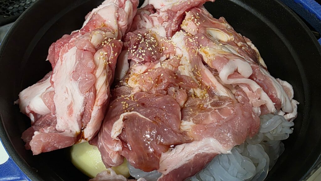 たまねぎ、じゃがいも、にんじんの上にさらにしらたきと豚こま切れ肉を乗せ、調味料をかけた状態。