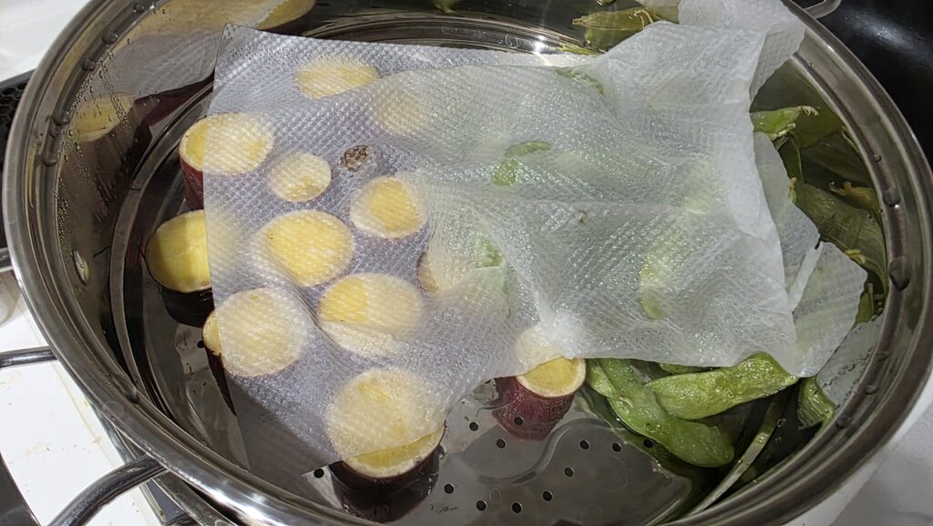 蒸し器の上にさつまいもと枝豆を乗せてキッチンペーパーで覆っている