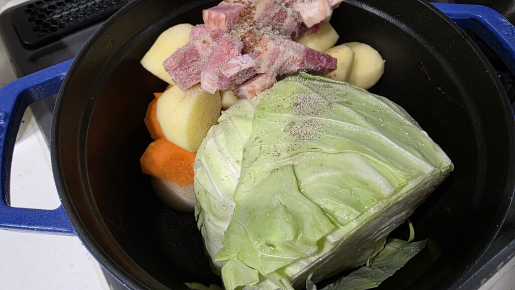 玉ねぎ、キャベツを鍋の底に敷いた上ににんじん、じゃがいも、ベーコンを乗せてコンソメと塩こしょうで味付けをした状態