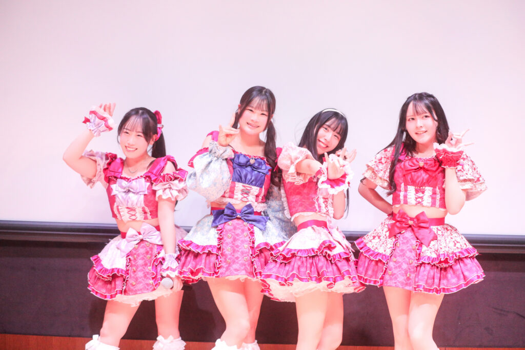 embellir(あんべりー)のライブ中の様子を撮影した写真。フツーに奇跡!!という楽曲のラストにある、横並びになるフォーメーション。
左から甘夏(あまなつ)あもちゃん、恋羽(こはね)あゆうちゃん、水野ひなたちゃん、遥乃(はるの)ももかちゃん。
それぞれ笑顔でポーズを決めている。