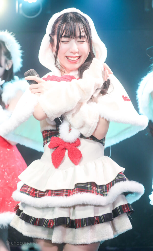 embellir(あんべりー)の水野ひなたちゃんをライブ中に撮影した写真。クリスマス当日という事で雪の妖精「ゆきんこ」の衣装を着ている。小指を立てて「約束」のポーズをしながら目を細めるくらい特大の笑顔をくれている。
2025年12月25日　GOTANDA G3　冠Fes Xmas SP！にて撮影。