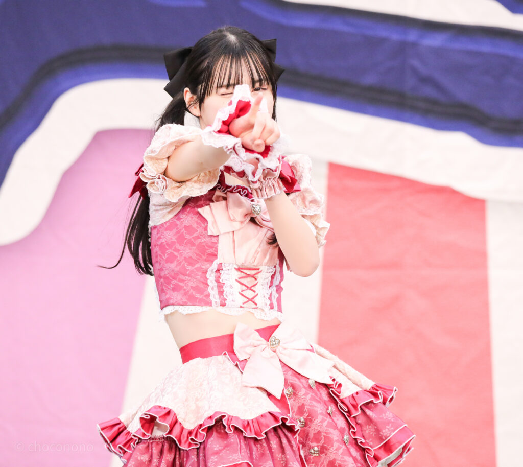 embellir(あんべりー)の水野ひなた(みずのひなた)ちゃんをライブ中に三列目真ん中あたりから撮影した写真。 ツインテールに黒い大きなリボン。 ベリーベリーの「必然的」の歌詞に合わせて小指を立ててこちらを見ながらウィンクしてくれている。 2026年1月25日上野水上音楽堂 超FREE BOMBER!!にて撮影