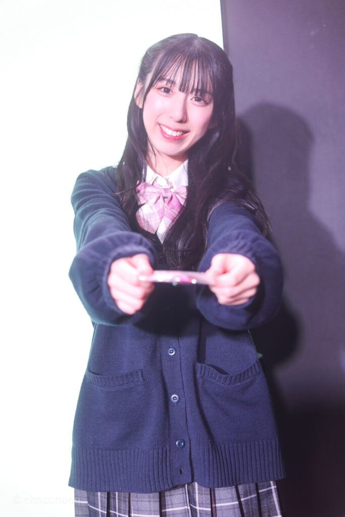 embellir(あんべりー)の水野ひなた(みずのひなた)ちゃんを特典会で撮らせてもらったソロショット写真。ひなたちゃんは制服にセーター。バレンタインにちなんで、チョコレートを渡そうとしてくれている。 2026年2月13日SHIBUYA ONE5　embellir presents VALENTINE LIVEにて撮影。