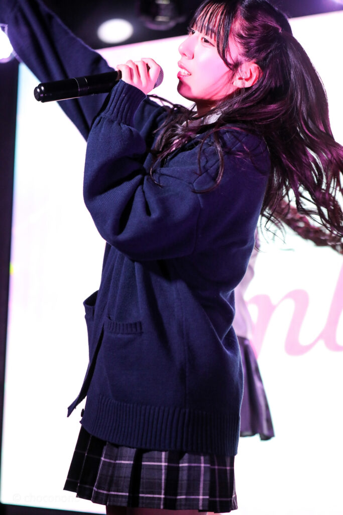 embellir(あんべりー)の水野ひなた(みずのひなた)ちゃんをライブ中に撮影した写真。ピンクリボンの制服に紺のセーター。 ダイナミックなダンスに合わせて髪が靡いている。 2026年2月13日SHIBUYA ONE5　embellir presents VALENTINE LIVEにて撮影。