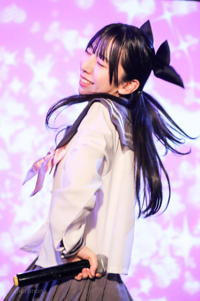 embellir(あんべりー)の水野ひなた(みずのひなた)ちゃんを最前列0番の位置からライブ中に撮影した写真。ピンクリボンのセーラー服にツインテールと大きな黒リボン。 笑顔で楽しそうにダンスしている。 2026年2月14日新宿DHNoA　IDOL FABRIC Valentineにて撮影。