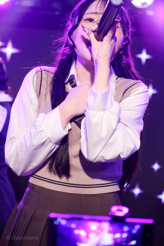 embellir(あんべりー)の遥乃ももか(はるのももか)ちゃんを最前列0番の位置からライブ中に撮影した写真。ブラウスに薄茶色のニットベスト。 落ちサビを熱唱している。 2026年2月14日新宿DHNoA　IDOL FABRIC Valentineにて撮影。