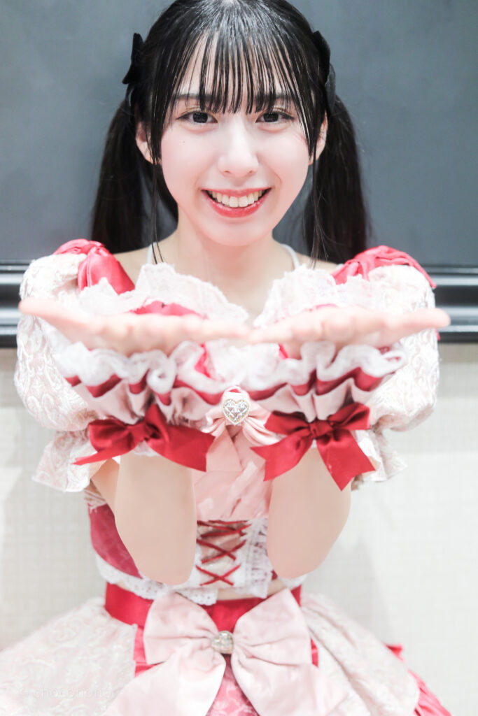 embellir(あんべりー)の水野ひなた(みずのひなた)ちゃんを特典会で撮らせてもらったソロショット写真。 ひなたちゃんは黒いリボンでツインテールにしている。 カメラに向かって投げキッスをしてくれている。 2026年2月21日GOTANDA G6　無銭ぷろじぇくと!!にて撮影。