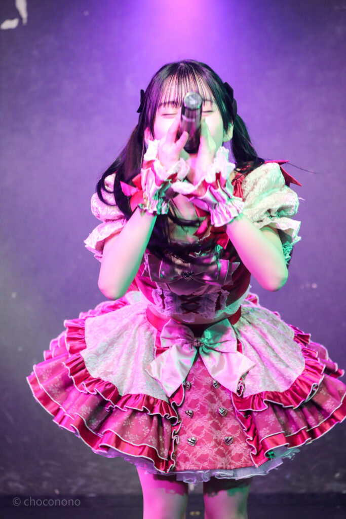 embellir(あんべりー)の水野ひなた(みずのひなた)ちゃんを最前列0番の位置からライブ中に撮影した写真。 黒いリボンでツインテールにしている。 フツーに奇跡!!の「出会えてよかったありがとう」の歌詞に合わせてお辞儀をしている。 2026年2月21日GOTANDA G6　無銭ぷろじぇくと!!にて撮影。