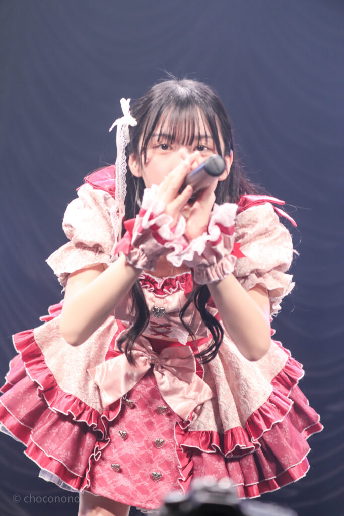 embellir(あんべりー)の水野ひなた(みずのひなた)ちゃんを最前列0番の位置からライブ中に撮影した写真。 ひなたちゃんは巻いた髪に白いリボンを着けている。 フツーに奇跡!!の「出会えてよかった　ありがとう」の歌詞に合わせてこちらを見つめながらお辞儀している。 2026年2月23日東京キネマ倶楽部　IDOL大博覧会にて撮影。