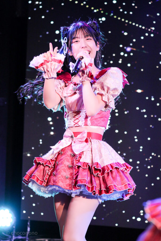 embellir(あんべりー)の水野ひなた(みずのひなた)ちゃんを最前列0番の位置から撮影したライブ写真。 ひなたちゃんは髪で猫耳を作っている。 にこにこと微笑みながらマイクを構えて歌唱している。 2026年2月22日中野坂上S.U.B Tokyo　妃Fesにて撮影。