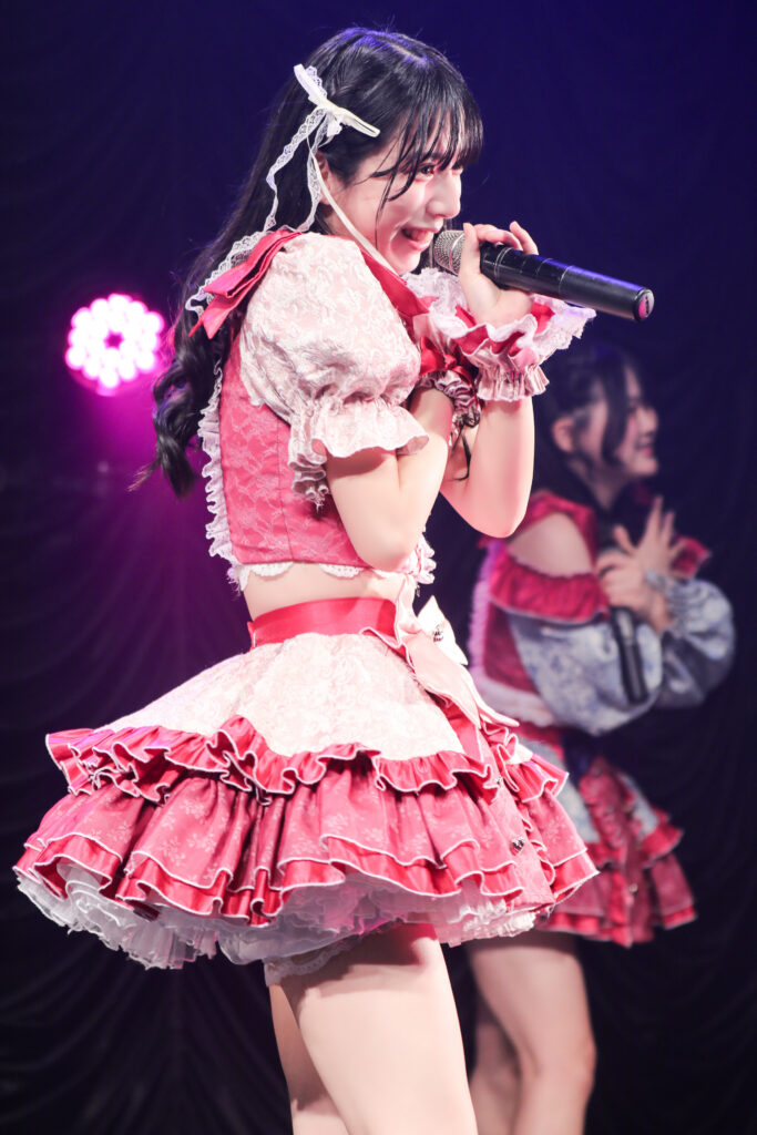 embellir(あんべりー)の水野ひなた(みずのひなた)ちゃんを最前列0番の位置からライブ中に撮影した写真。 フツーに奇跡!!の「ずっと　ずっとずっと」の歌詞に合わせて自分の肩を抱きながら歌唱している。 2026年2月23日　東京キネマ倶楽部　IDOL大博覧会にて撮影