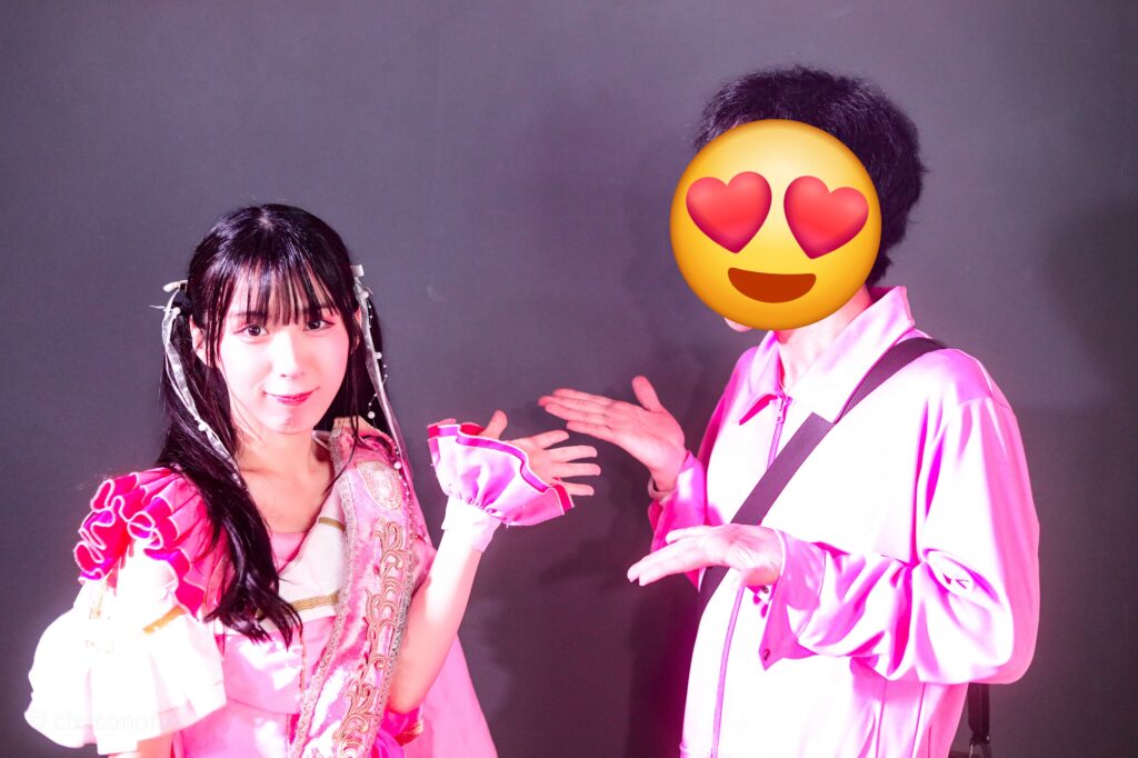 embellir(あんべりー)の水野ひなた(みずのひなた)ちゃんと特典会で撮ってもらったツーショット写真。 ひなたちゃんはツインテールに白のリボン、姉妹グループ瞬きもせずの襷衣装のピンクを着ている。今は卒業してしまった元推しメン、琴音ゆあちゃんが当時着ていたもの。 お互いの方を手で指し示して衣装アピールし合っている。 2026年3月3日SHIBUYA ONE5　embellir presentsひなまつりにて撮影。