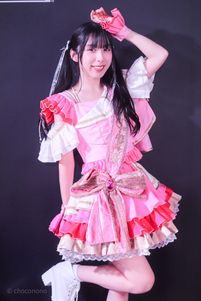 embellir(あんべりー)の水野ひなた(みずのひなた)ちゃんを特典会で撮らせてもらったソロショット写真。 ひなたちゃんはツインテールに白のリボン、姉妹グループ瞬きもせずの襷衣装のピンクを着ている。今は卒業してしまった元推しメン、琴音ゆあちゃんが当時着ていたもの。 頭に手を置いて片足を上げてモデルのようにポーズを決めてくれている。 2026年3月3日SHIBUYA ONE5　embellir presentsひなまつりにて撮影。