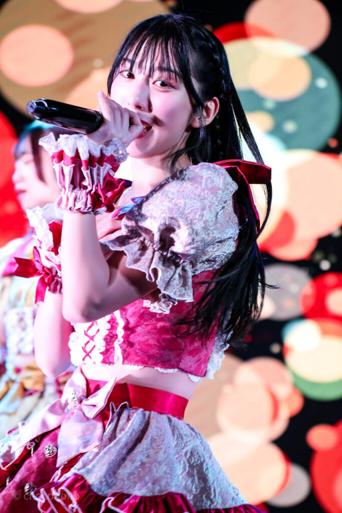 embellir(あんべりー)の水野ひなた(みずのひなた)ちゃんを最前列0番の位置からライブ中に撮影した写真。 ひなたちゃんは髪を編み込んでいる。 ダンスをしながらマイクを構えて歌唱している カラフルなバックスクリーンとひなたちゃんの笑顔がとても綺麗で印象的。 2026年3月1日中野坂上S.U.B Tokyo NIPPON MUSIC JAM!!miniにて撮影。