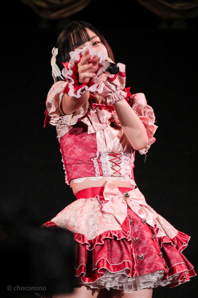 embellir(あんべりー)の水野ひなた(みずのひなた)ちゃんを最前列0番の位置からライブ中に撮影した写真。 ひなたちゃんはストレートヘアーに白のリボンを着けている。 ベリーベリーの「可愛いが欲しいの」の歌詞に合わせてこちらに手を伸ばしてほしがりポーズ。 2026年3月8日新世紀ホール　iCOLONY iDOL LiVEにて撮影