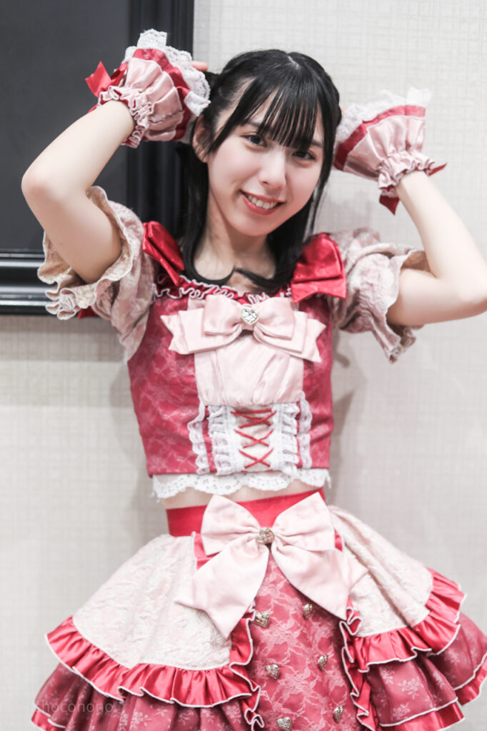 embellir(あんべりー)の水野ひなた(みずのひなた)ちゃんを特典会で撮らせてもらったソロショット写真。 ひなたちゃんは編み込みに黒いリボンを着けている。 リボンに手を添えてニューヘアーをアピールしてくれている。 2026年3月7日GOTANDA G6　無銭ぷろじぇくと!!にて撮影。