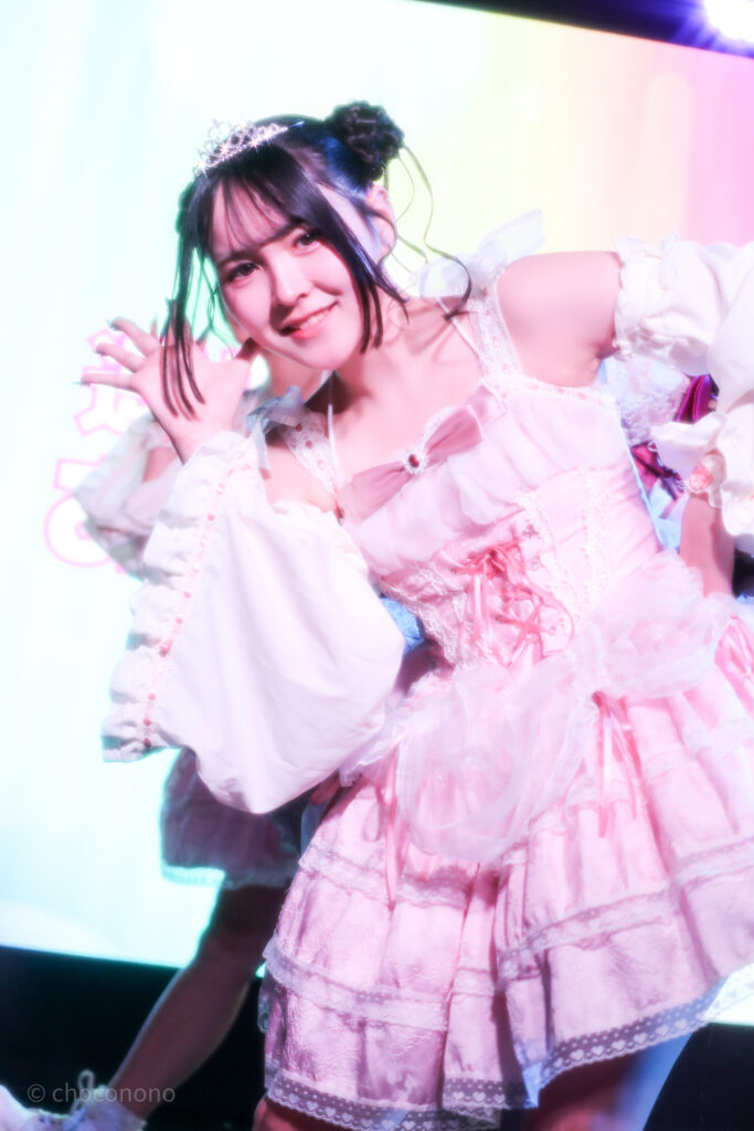 embellir(あんべりー)の遥乃ももか(はるのももか)ちゃんを最前列下手2番あたりから撮ったライブ写真。 生誕衣装のピンクのドレスを着て、ティアラを着けている。羊さんヘアー。 こちらに視線を向けながら顔の横で手のひらを広げてポーズを決めている。 2026年3月14日SHIBUYA ONE5　遥乃ももか×恋羽あゆうおたんじょうびかいにて撮影