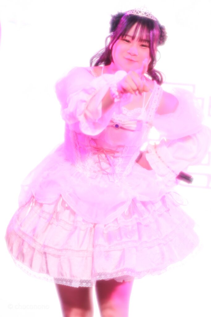 embellir(あんべりー)の恋羽あゆう(こはねあゆう)ちゃんを最前列下手2番あたりから撮ったライブ写真。 生誕衣装のピンクのドレスを着て、ティアラを着けている。羊さんヘアー。 ちょんとつつくような仕草をしている。 2026年3月14日SHIBUYA ONE5　遥乃ももか×恋羽あゆうおたんじょうびかいにて撮影