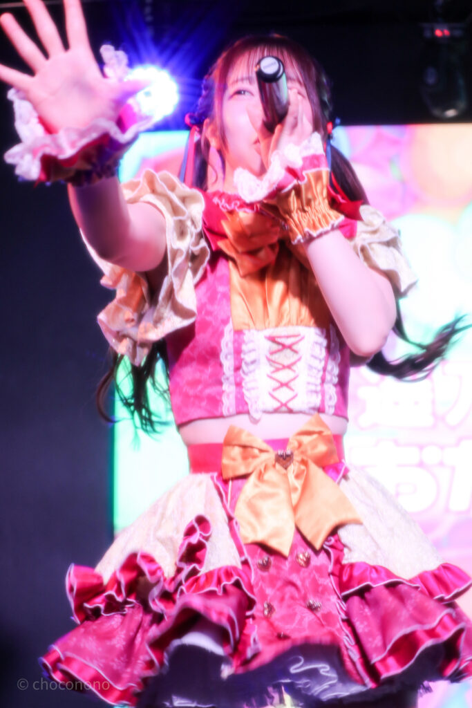 embellir(あんべりー)の泡沫あおい(うたかたあおい)ちゃんを最前列下手2番あたりから撮ったライブ写真。 真ん中あたりでツインテールにして赤と青のリボンで結んでいる。 手のひらを前にかざし、マイクを構えて歌唱している。 2026年3月14日SHIBUYA ONE5　遥乃ももか×恋羽あゆうおたんじょうびかいにて撮影