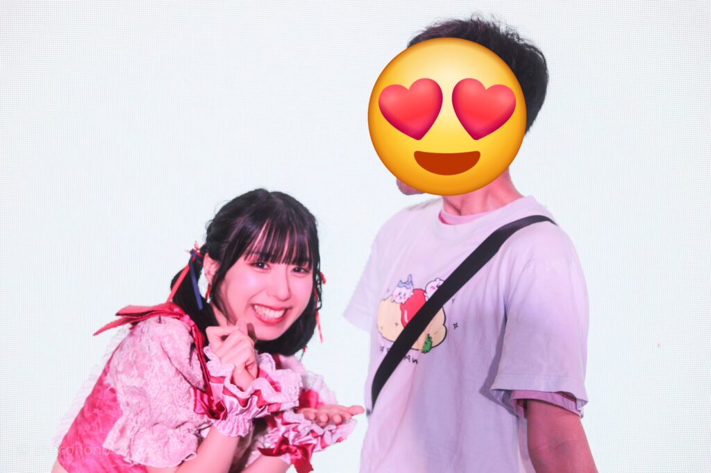 embellir(あんべりー)の水野ひなた(みずのひなた)ちゃんと特典会で撮影してもらったツーショット写真。 ひなたちゃんは真ん中あたりのツインテールを赤と青のリボンで結んでいる。 お皿と食器を持って私の胸元にプリントされたオムライスを食べようとしているジェスチャー。 にこにこしている。 2026年3月14日SHIBUYA ONE5　遥乃ももか×恋羽あゆうおたんじょうびかいにて撮影