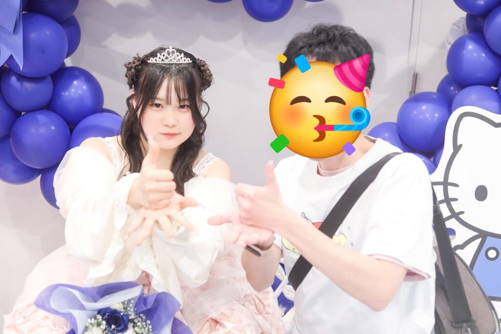 embellir(あんべりー)の恋羽あゆう(こはねあゆう)ちゃんと特典会で撮ってもらったツーショット写真。 あゆうちゃんは生誕衣装のピンクのドレスを着ている。頭にはティアラを乗せている。 二人で片方の手のひらにサムズアップした手を乗せて「お誕生日ポーズ」 2026年3月14日SHIBUYA ONE5　遥乃ももか×恋羽あゆうおたんじょうびかいにて撮影。