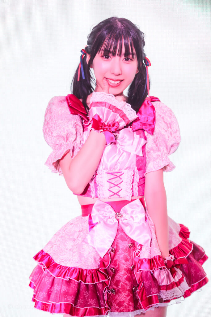 embellir(あんべりー)の水野ひなた(みずのひなた)ちゃんを特典会で撮らせてもらったソロショット写真。 ひなたちゃんは真ん中あたりのツインテールを赤と青のリボンで結んでいる。 親指を口元に持っていって「ばぶちゃんポーズ」 2026年3月14日SHIBUYA ONE5　遥乃ももか×恋羽あゆうおたんじょうびかいにて撮影