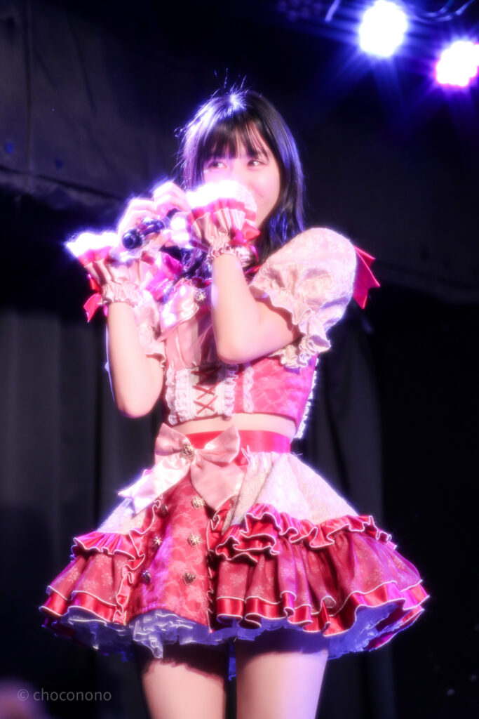 embellir(あんべりー)の水野ひなた(みずのひなた)ちゃんを最前列0番の位置からライブ中に撮影した写真。 ひなたちゃんはストレートヘアーをベースに一束髪を編んでいる。 フロア後方に向けて手でハートを作って送っている。レンズフィルターの効果で光の当たった部分がキラキラと輝いている。 2026年3月15日中野坂上S.U.B Tokyo　妃Fesにて撮影。