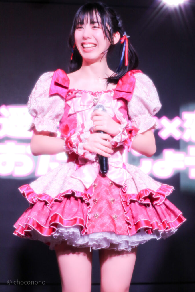 embellir(あんべりー)の水野ひなた(みずのひなた)ちゃんを最前列下手2番あたりから撮ったライブ写真。 真ん中あたりでツインテールにして赤と青のリボンで結んでいる。 MC中、にこにことフロアのどこかに視線を向けている。 2026年3月14日SHIBUYA ONE5　遥乃ももか×恋羽あゆうおたんじょうびかいにて撮影