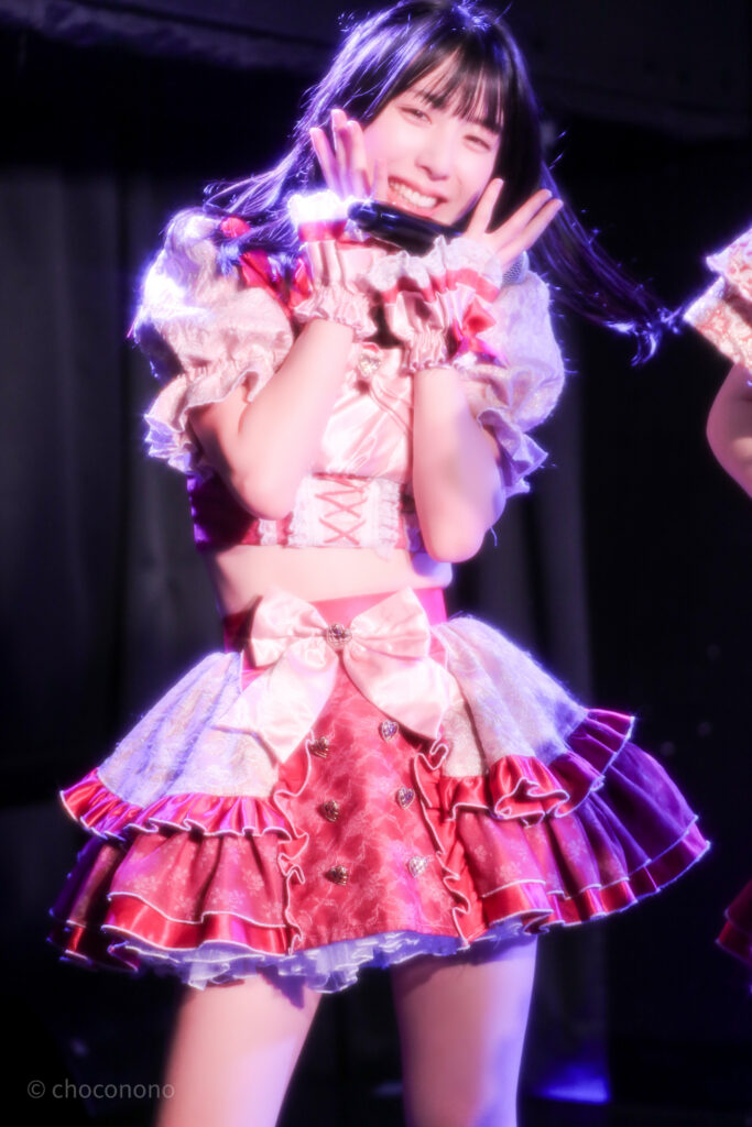 embellir(あんべりー)の水野ひなた(みずのひなた)ちゃんを最前列0番の位置からライブ中に撮影した写真。 ひなたちゃんはストレートヘアーをベースに一束髪を編んでいる。 MC中、カメラを向けているのに気づいて愛嬌を振りまいてくれている。 2026年3月15日中野坂上S.U.B Tokyo　妃Fesにて撮影。