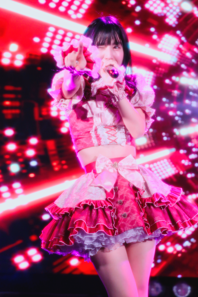 中野坂上S.U.B Tokyoでembellir（あんべりー）の水野ひなた（みずのひなた）ちゃんをEOS 5D Mark IVとEF70-300mm（120mm）で縦位置に撮ったライブ写真。赤いLEDスクリーンを背景に、ウインクしながらこちらを指差している。1/200、F4.5、ISO 1250。