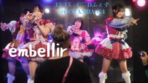 embellirメンバーが横並びになってそれぞれフロアの一点を指さしているシーンのスクリーンショット。グループ名とイベント詳細のテキストを埋め込んでいる。