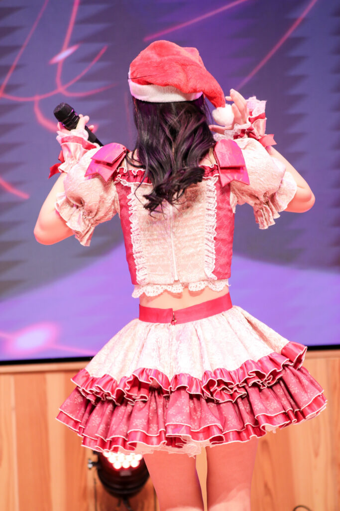 embellir(あんべりー)の水野ひなたちゃんをライブ中に撮影した後ろ姿の写真。
この日はクリスマスイベントということでひなたちゃんはサンタの帽子をかぶっている。
帽子の下から見える後ろ髪は巻かれていてとても大人っぽい魅力を醸し出している。
2025年12月14日　としま区民センター多目的ホール　IDOL SODA Stream!!にて撮影。