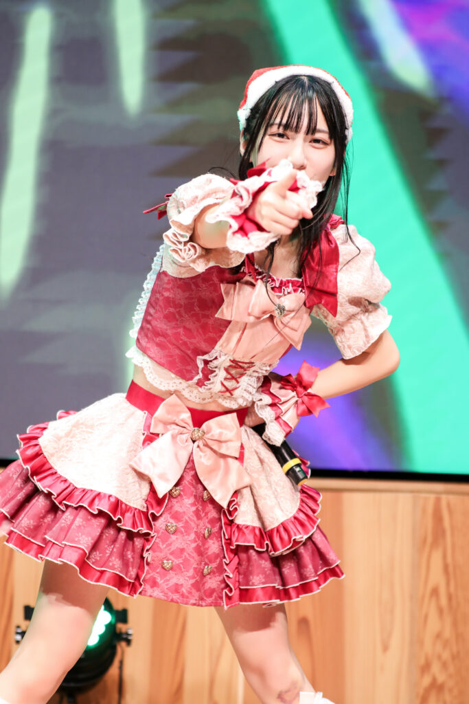 embellir(あんべりー)の水野ひなたちゃんをライブ中に撮影した写真。
この日はクリスマスイベントということでひなたちゃんはサンタの帽子をかぶっている。
こちらを真っ直ぐ見つめて指さしてくれている。
2025年12月14日　としま区民センター多目的ホール　IDOL SODA Stream!!にて撮影。